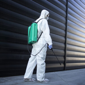 Person in white chemical protection suit doing disinfection and pest control with sprayer to kill insects and rodents.